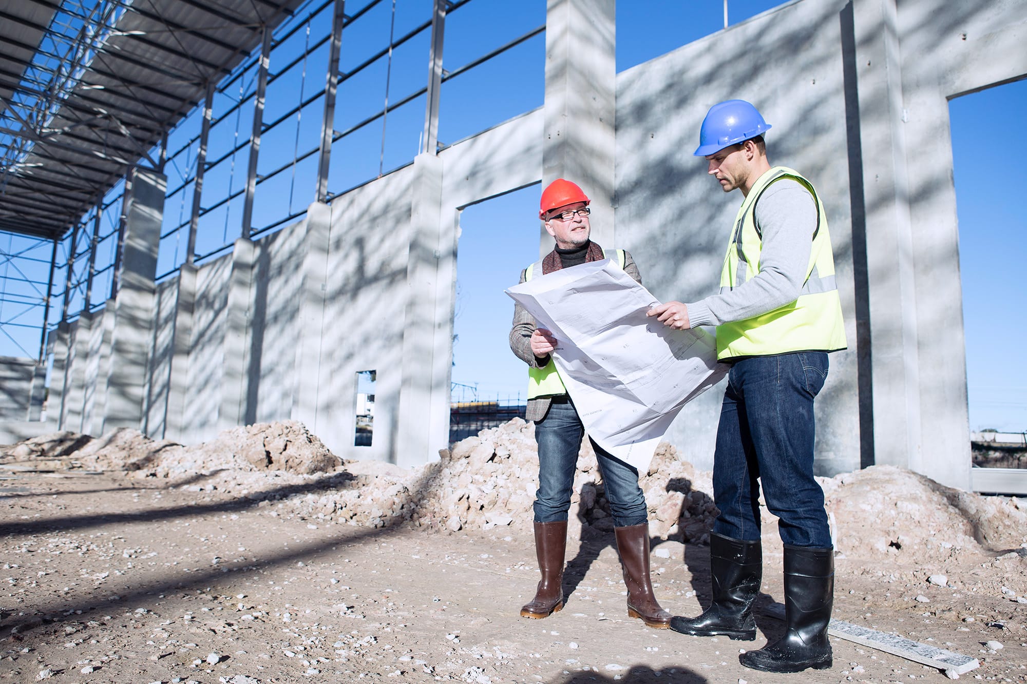 Two workers at a construction site reviewing blueprints
