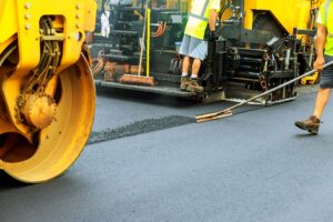 Workers using roller machinery to pave a road with blacktop