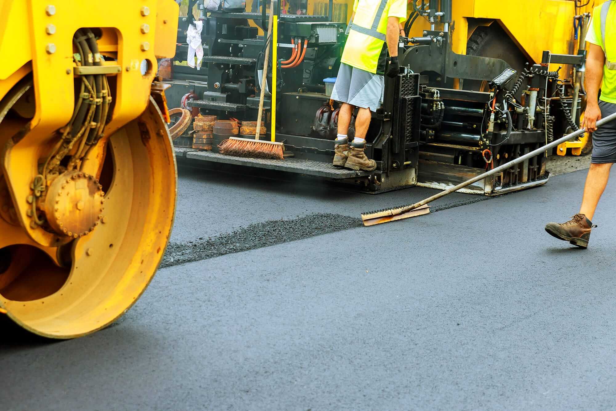 Workers using roller machinery to pave a road with blacktop